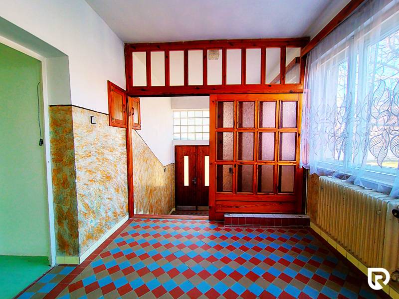 Ein Flur in einem Einfamilienhaus mit Fliesen in buntem Muster, Holztüren und Vorhängen.