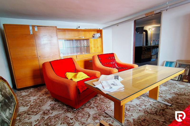 Ein Wohnzimmer in einem Einfamilienhaus mit älteren Sesseln, einem Tisch und einem Glasschrank.