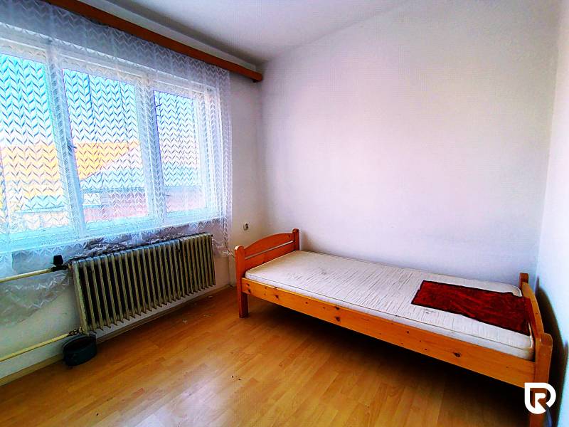 Einzelzimmer mit Bett und Fenster, Boden mit Holzdekor, in einem Einfamilienhaus.