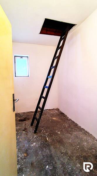 Dachboden in einem Einfamilienhaus mit einer Leiter, die zu einer Öffnung in der Decke führt.