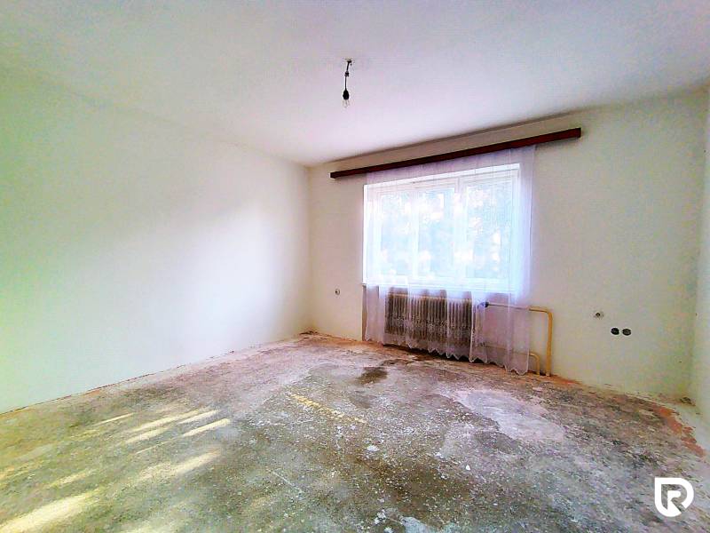 Ein leerer Raum in einem Einfamilienhaus mit abgenutztem Boden, Heizkörper und Vorhängen.