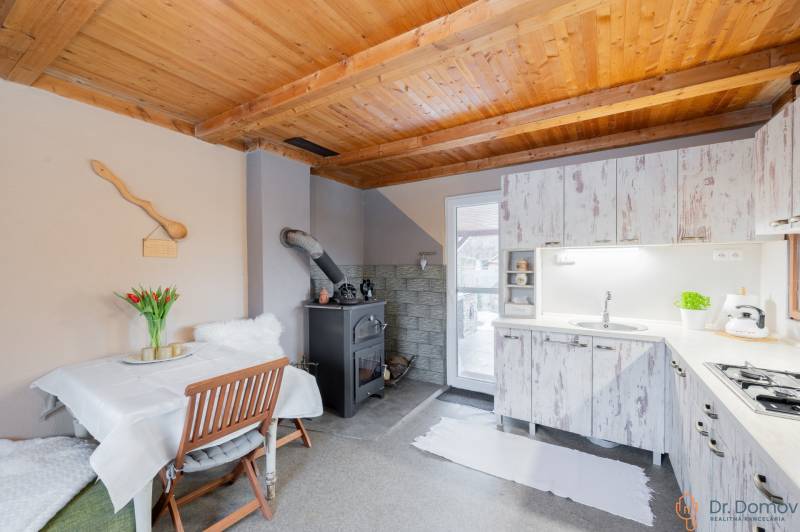 Küche in einer Hütte mit Holzdecke, Ofen und weißen Möbeln.