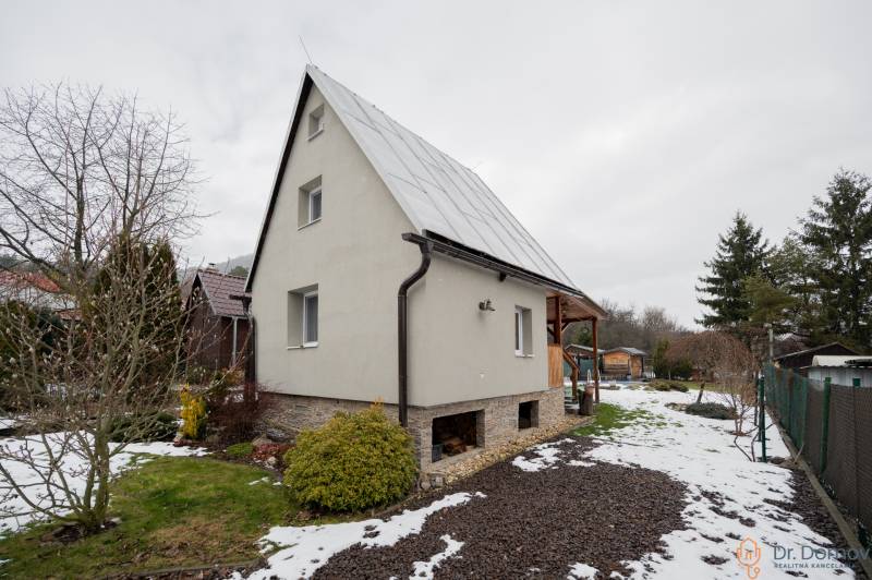 Ein Haus in Handlová mit Rasen und einem verschneiten Garten, umgeben von Bäumen und Sträuchern.