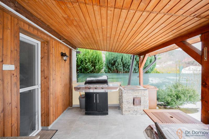 Holzverkleidung und Grill auf der Terrasse der Hütte in Handlová, neben grünen Sträuchern.