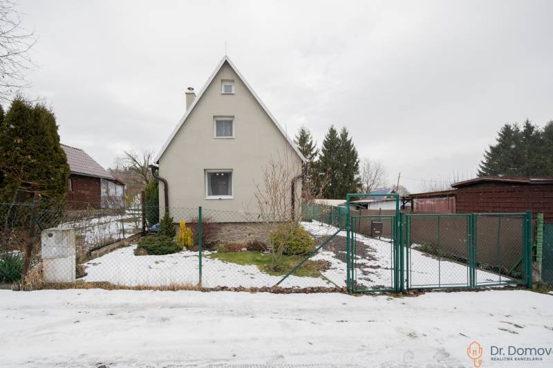 Ein Haus in Handlová mit etwas Schnee im Hof, umgeben von Grün und einem Zaun.