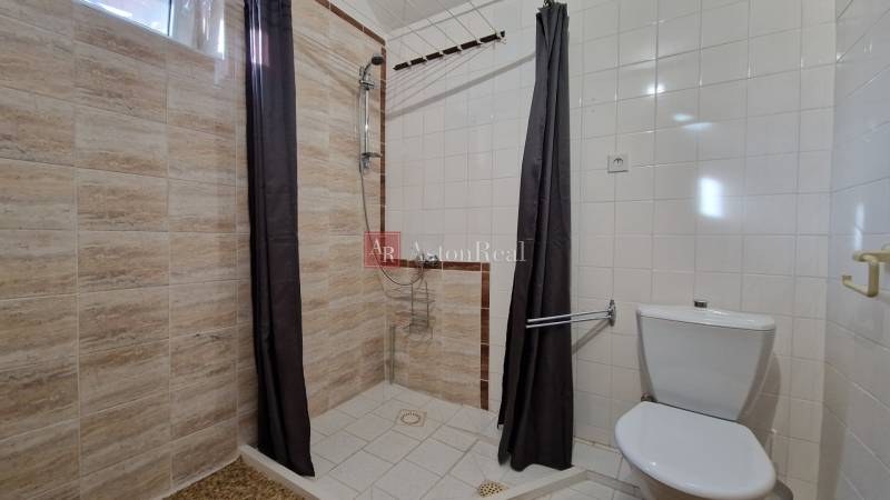 Ein Badezimmer in einem Einfamilienhaus mit einer einfachen Duschkabine und hellen Fliesen.