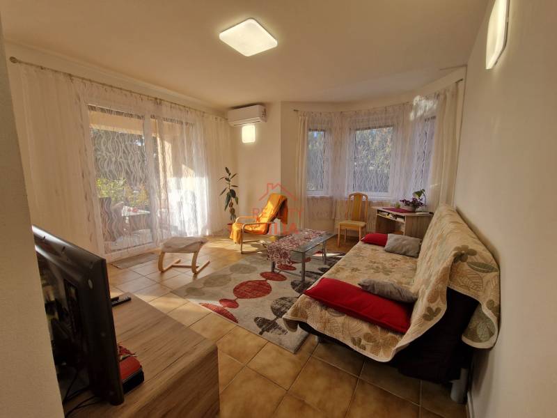 Obývací pokoj rodinného domu s televizí, pohovkou, stolkem a velkými okny se závěsy.