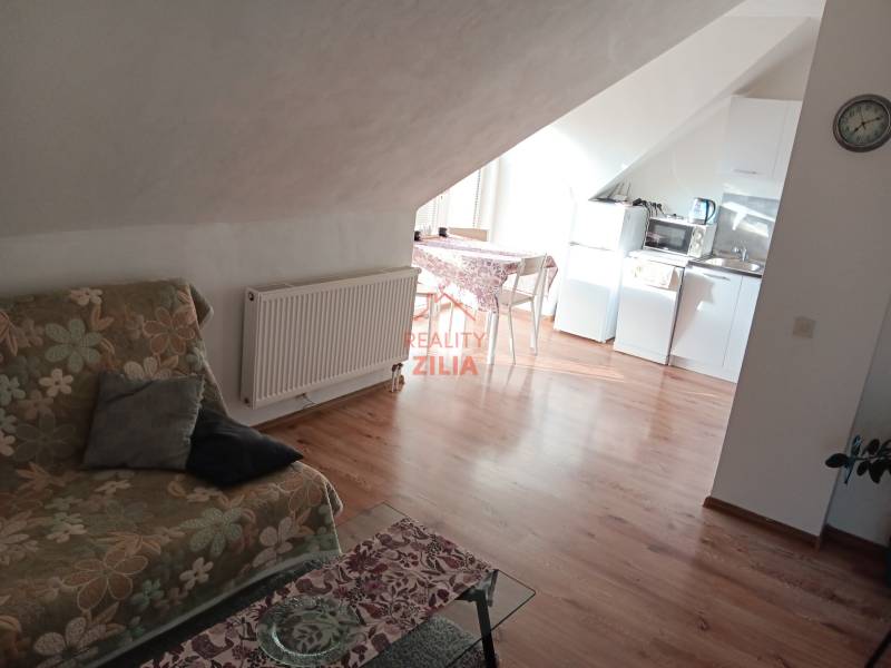 Dachboden in einem Einfamilienhaus mit Küche, einem Blumenmuster-Sofa und einem Boden in Holzoptik.