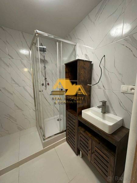 Badezimmer in einer 2-Zimmer-Wohnung mit weißen Fliesen, einer Duschkabine und einem Waschbecken auf einem Schrank.