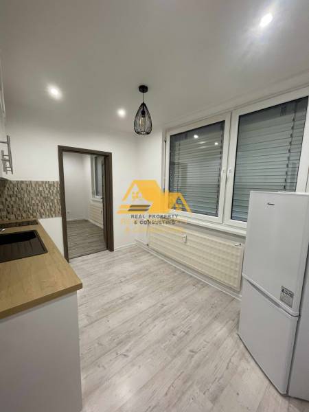 Küche in einer Einzimmerwohnung mit Holzboden und weißen Elektrogeräten.