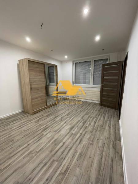 Geräumiges Zimmer mit einem Schiebeschrank und einem Boden mit Holzdekor in einer Einzimmerwohnung.