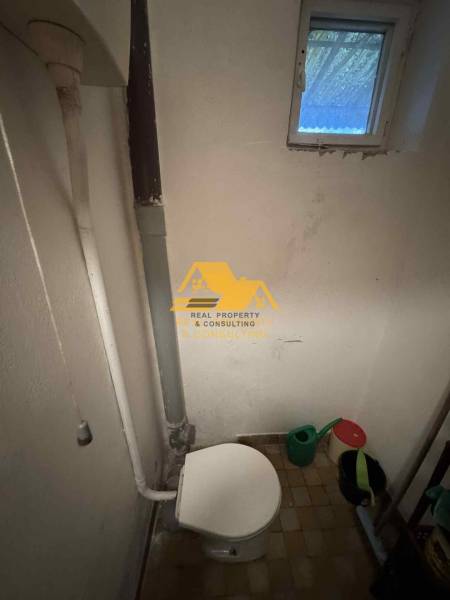 Badezimmer im Einfamilienhaus mit Toilette und kleinem Fenster, Eimer und Gießkanne.