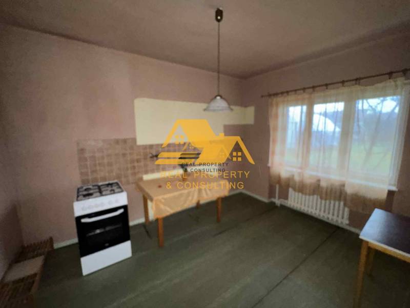 Eine Küche in einem Einfamilienhaus mit einem Herd, einem Tisch, einer Gardine und einer hellen Wanddekoration.