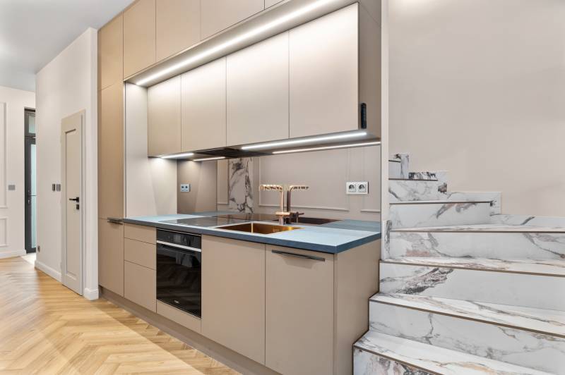 Küche in einer 2-Zimmer-Wohnung mit Marmortreppe und Boden in Holzoptik.