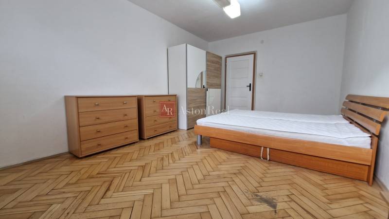Schlafzimmer in einer 2-Zimmer-Wohnung mit Holzdekor auf dem Boden, Bett und Kommoden.