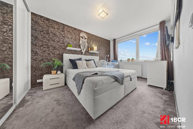 Schlafzimmer in einer 2-Zimmer-Wohnung mit Doppelbett, Teppichboden und dekorativer Wand.