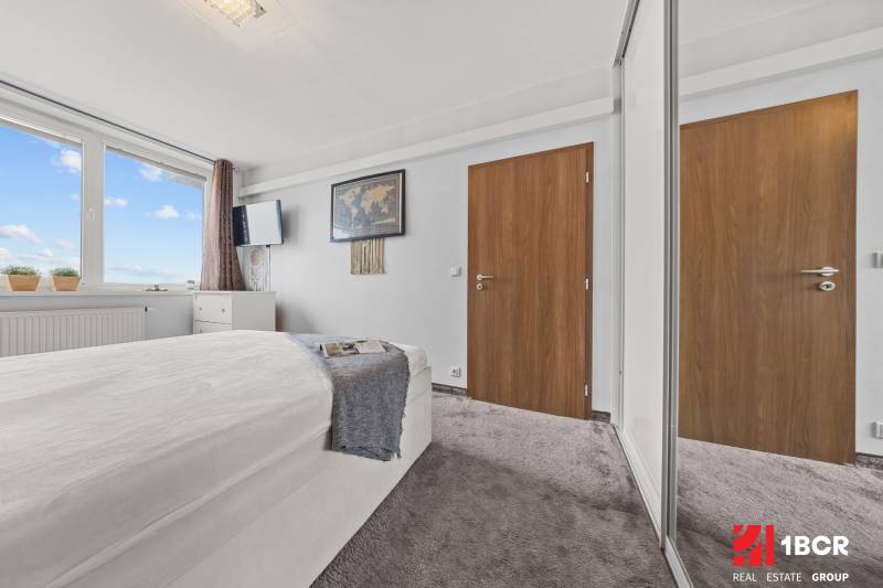 Helles Schlafzimmer mit Bett, großem Fenster und Kleiderschrank in einer 2-Zimmer-Wohnung.