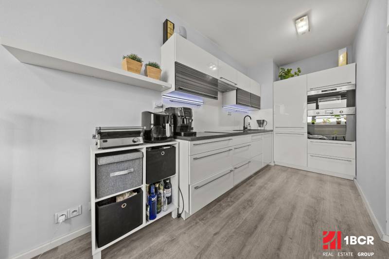 Küche in einer 2-Zimmer-Wohnung mit weißen Schränken und einem Boden in Holzoptik.