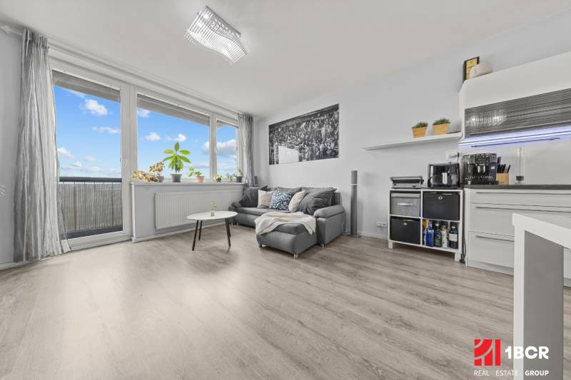 Wohnbereich einer 2-Zimmer-Wohnung mit Sofa, Tisch und Boden in Holzoptik.