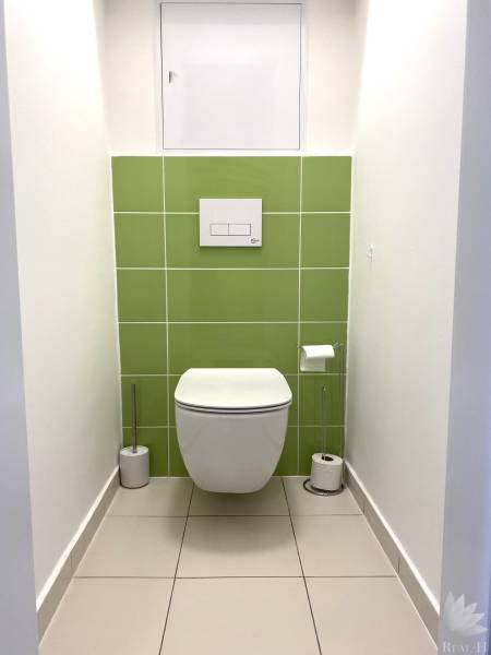 Toilette mit weißen und grünen Fliesen in einer 3-Zimmer-Wohnung.