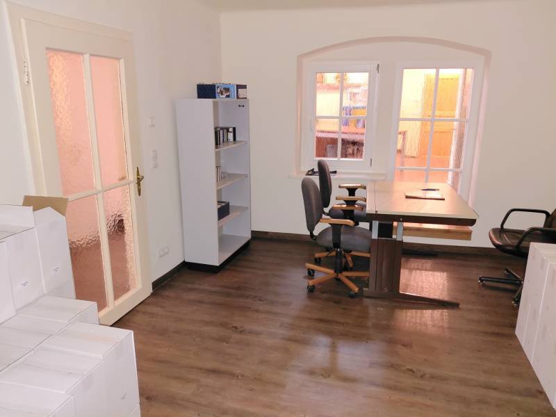 Ein Büro mit einem Fenster, einem Regal, zwei Stühlen und einem Boden mit Holzdekor.