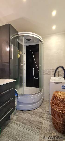 Badezimmer in einer 2-Zimmer-Wohnung mit Duschkabine und Waschmaschine, Fliesen mit Holzdekor.