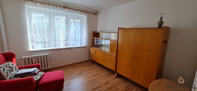 Ein Zimmer in einer 3-Zimmer-Wohnung mit älteren Möbeln und einem Boden in Holzoptik.