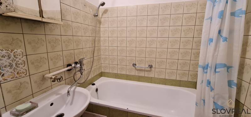 Ein Badezimmer mit Spiegel und Badewanne in einer 3-Zimmer-Wohnung, gefliest mit dekorativen Fliesen.