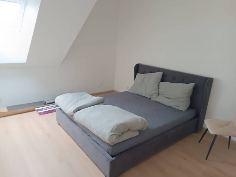 Schlafzimmer in einer Zweizimmerwohnung mit Bett, Holzboden und Dachfenster.