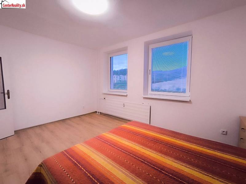 Helles Zimmer mit zwei Fenstern, einem Bett und einem Boden mit Holzdekor.