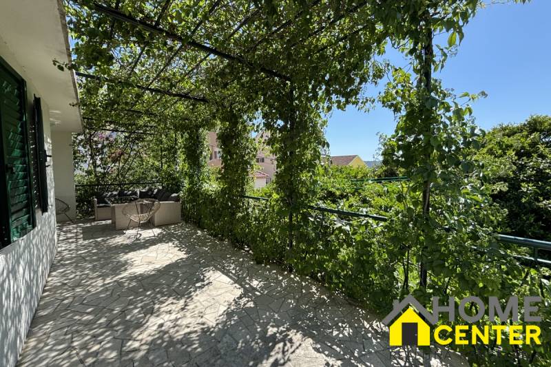 Die Terrasse eines Einfamilienhauses in Čiovo mit einer von Grün überwachsenen Pergola und einer Außensitzgelegenheit.