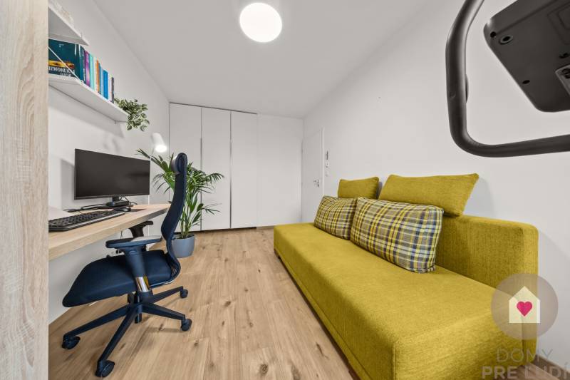 Ein Zimmer in einer 4-Zimmer-Wohnung mit einem grünen Sofa, einem Computer und einem Boden mit Holzdekor.