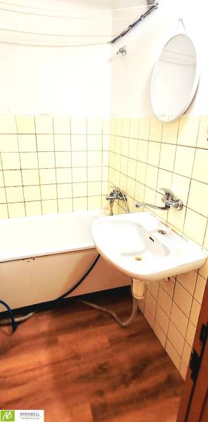Badezimmer mit Badewanne, Waschbecken und Boden mit Holzdekor in einer 3-Zimmer-Wohnung.