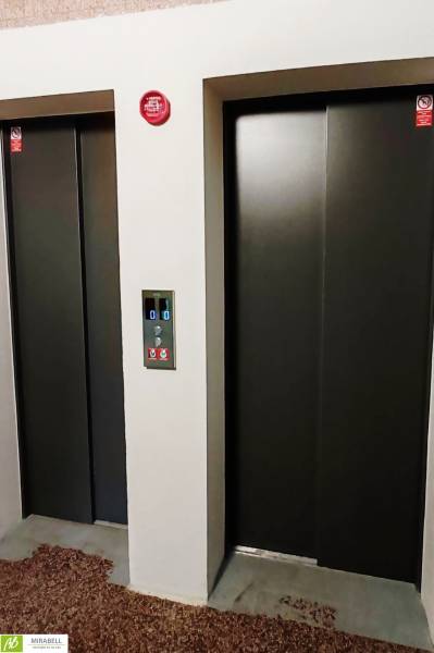 Zwei Aufzüge mit Metalltüren und einem Bedienfeld dazwischen.