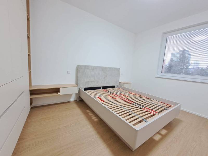 Schlafzimmer in einer 2-Zimmer-Wohnung mit Holzboden, großem Fenster, Bett und Stauraum.