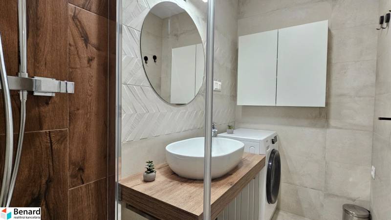 Badezimmer in einer Einzimmerwohnung mit Waschbecken, Dusche und Waschmaschine, Boden mit Holzdekor.