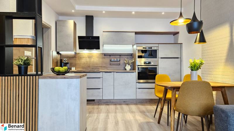 Küche in einer Einzimmerwohnung mit Holzboden, Esstisch und gelben Stühlen.