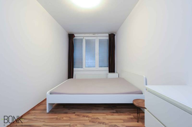 Schlafzimmer in einer 2-Zimmer-Wohnung mit weißen Möbeln und einem Boden in Holzoptik.