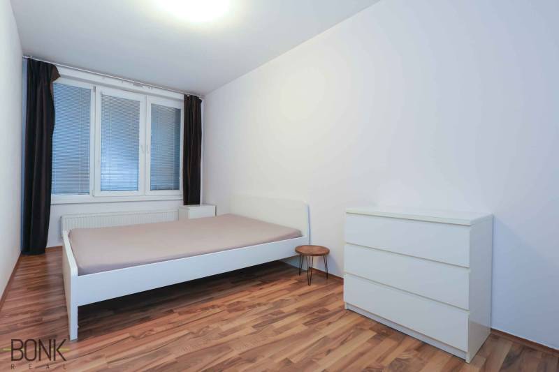 Schlafzimmer in einer 2-Zimmer-Wohnung mit Bett, Kommode und Boden in Holzoptik.