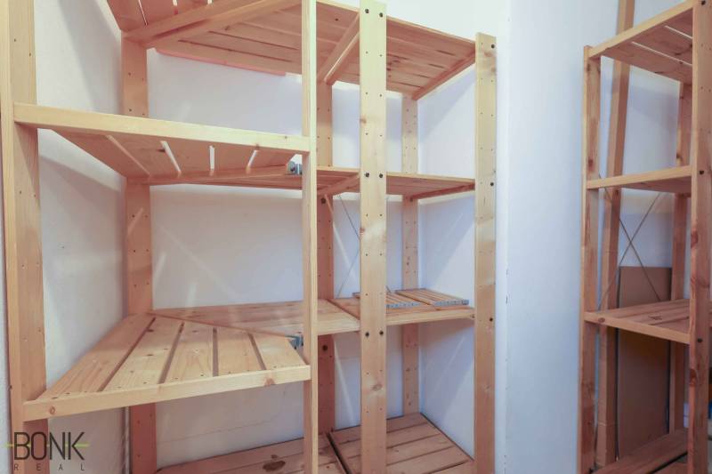 Holzregale in der Speisekammer einer Zweizimmerwohnung mit weißen Wänden.