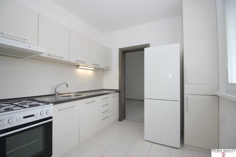 Küche in einer 3-Zimmer-Wohnung mit weißen Schränken und weißem Boden.