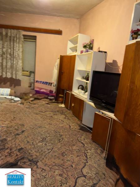 Ein Zimmer in einem Einfamilienhaus mit Teppich, Regalen, Fernseher und Vorhängen.