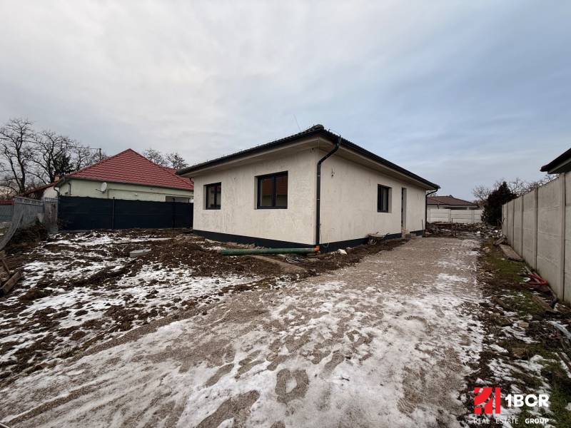 Ein Einfamilienhaus in Senec mit einem ungepflegten, verschneiten Grundstück und einem Betonweg.