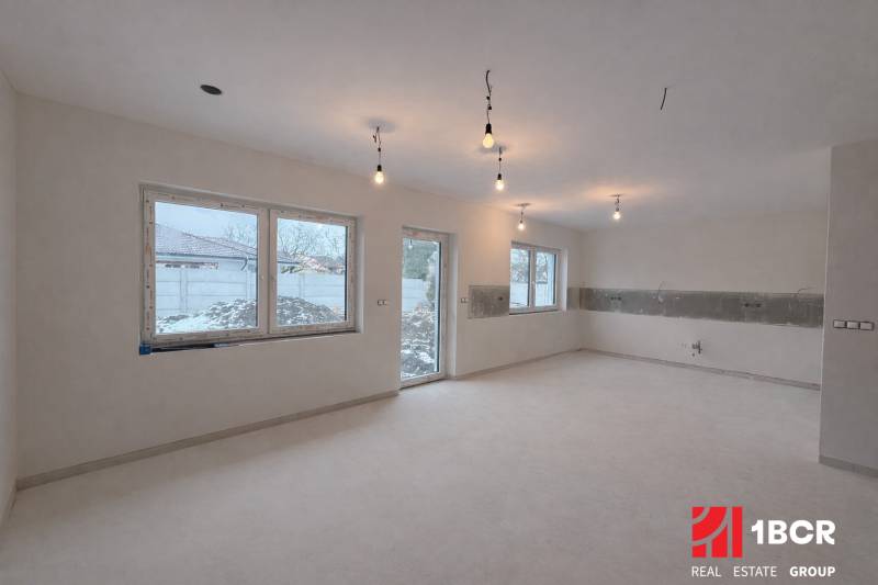 Innenraum in einem Einfamilienhaus mit hellem Boden und großen Fenstern, ohne Möbel.