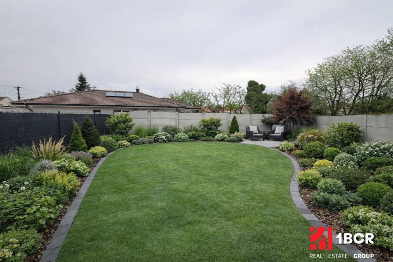 Ein gepflegter Garten mit Terrasse eines Einfamilienhauses in Veľký Grob, reich an Grün und Bepflanzung.