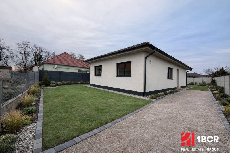Ein Einfamilienhaus in Veľký Grob mit Rasen, einem Kiesweg und einem gepflegten Garten.