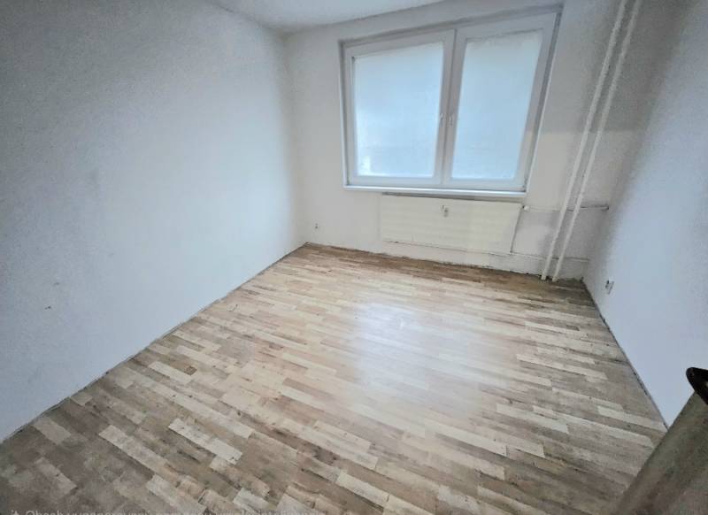 Ein leerer Raum mit weißen Wänden und einem Boden in Holzoptik in einer 3-Zimmer-Wohnung.