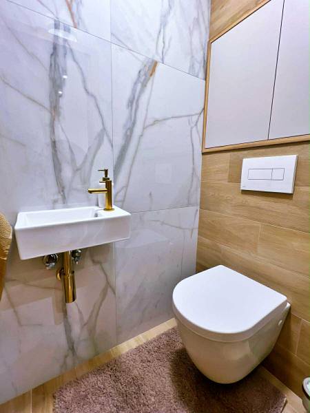 Badezimmer mit Keramikwaschbecken, Spiegel und Boden mit Holzdekor in einer 3-Zimmer-Wohnung.