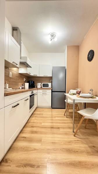 Küche in einer 2-Zimmer-Wohnung mit weißen Schränken und einem Boden in Holzoptik.