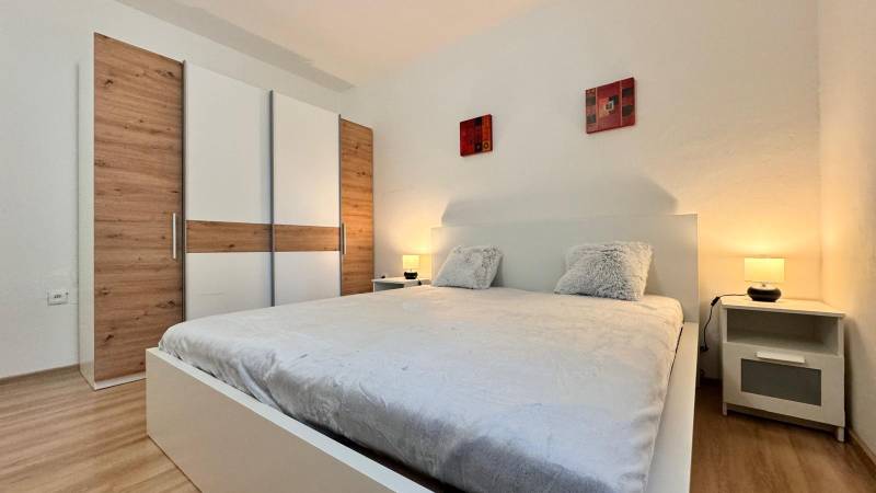 Schlafzimmer in einer 2-Zimmer-Wohnung mit einem großen Bett, einem Kleiderschrank und einem Boden mit Holzdekor.